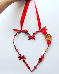 a hand holding a heart shaped beaded necklace with red ribbon and buttons on it