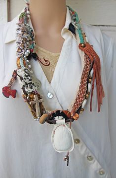 This large lightweight fabric and leather necklace is new, handmade, and one of a kind.  It slips easily over the head and is 34" around, made of different fabrics and textiles, suede and leathers.  I beaded this necklace with beads made of wood, bone, shells, cowry shells, brass, glass, plastic, and faux pearls. I added a black bow charm, a silver charm with a branch impression, a flying dove, and a painted vintage Mexican fish charm. There is also a small wooden cross, woven beaded leather, and a white leather fob that I made after looking at rustic African Akan jewelry from about 1950. This necklace is photographed being worn by a lifesize mannequin, and also next to a ruler. It is new and was made in a smoke-free environment. It has a very eclectic Bohemian feel, and looks elegant when Bohemian Leather Necklace For Festivals, White Leather Bohemian Jewelry, White Bohemian Leather Jewelry, Bohemian White Leather Jewelry, Mexican Fish, Flying Dove, Leather Fob, Textile Necklace, Bohemian Festival