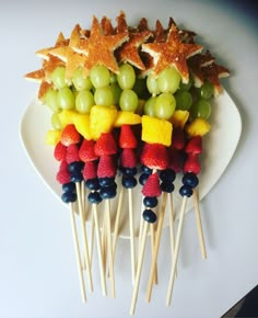 fruit skewers are arranged on a plate with star shaped candies and grapes