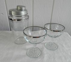 three glass bowls with lids are sitting on a white tablecloth next to a shaker