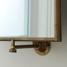 a mirror mounted to the side of a white wall next to a metal pipe and hook