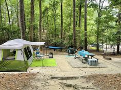 a tent set up in the middle of a forest with picnic tables and hammocks