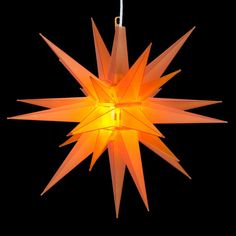 an origami star hanging from a string on a black background with the light turned on