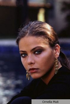 a beautiful young woman with long hair and earrings on her head looking at the camera