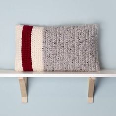 a knitted pillow sitting on top of a white shelf next to a blue wall