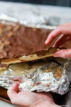 a person is taking some food out of a foil wrapper on top of a table