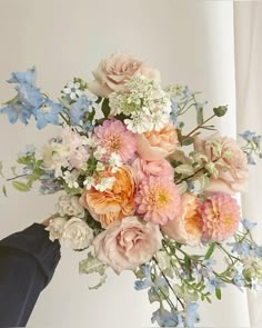 a bouquet of flowers is being held up by someone's hand in front of a white wall