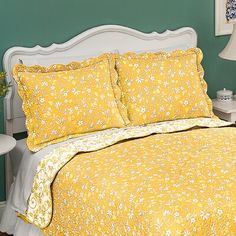 a bed with yellow comforter and pillows in a room next to a lamp on a table