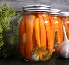 four jars filled with carrots and garlic on a table next to an onion bulb