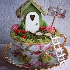 a teacup with a birdhouse in it on top of a saucer filled with flowers