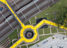 an aerial view of a yellow object in the middle of a parking lot next to train tracks