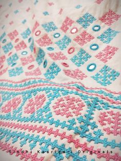 a close up of a blanket with blue and pink crocheted designs on it