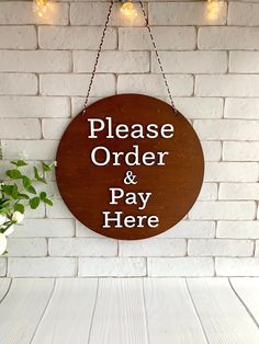 a sign that says please order and pay here hanging on a brick wall next to a potted plant