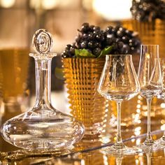 several wine glasses and a decanter on a table with grapes in the background