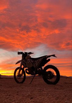 a dirt bike parked on top of a dry grass field under a colorful sky at sunset