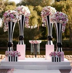 three tall black and white vases with flowers on each one stand at an outdoor ceremony