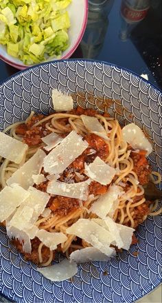 a blue and white plate topped with pasta next to a bowl of lettuce