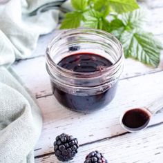 blackberry jam in a glass jar with two blackberries next to it on a white wooden table