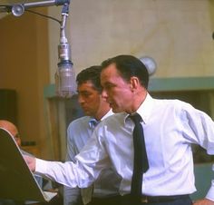 two men in dress shirts and ties are looking at a computer screen while standing next to a microphone