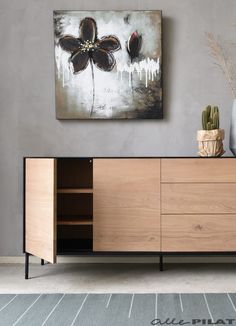 a painting hanging on the wall above a wooden cabinet with two plants in vases