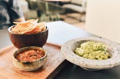 some guacamole chips and salsa on a wooden tray at a restaurant table