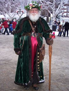 a man dressed in green and red standing next to a wooden stick