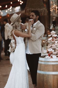 a man and woman standing next to each other in front of a wooden barrel eating cake