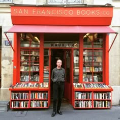 a man standing in front of a book store with red bookshelves full of books