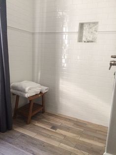 a white tiled bathroom with wood flooring and wooden stool next to the shower curtain