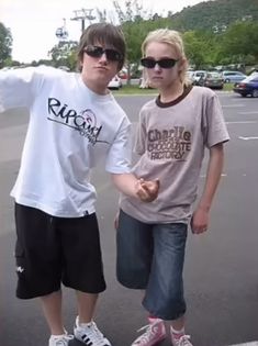 two young people standing next to each other in a parking lot with their arms outstretched