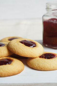 several cookies with jam on them sitting next to a jar