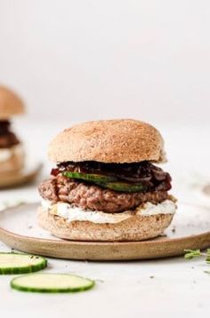 a hamburger on a plate with pickles around it and another burger in the background