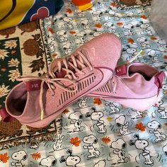 a pair of pink tennis shoes sitting on top of a bed covered in cartoon characters