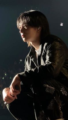 a young man sitting on top of a wooden bench in front of a crowd at night