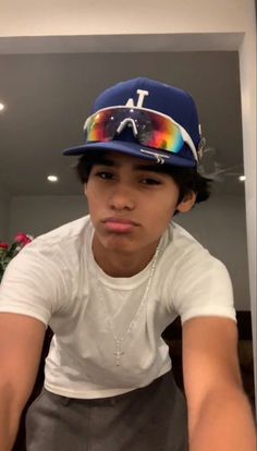 a young boy wearing a hat and glasses in front of a mirror with his tongue out