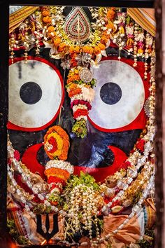 an elaborately decorated mask with eyes and flowers on display at a temple in india