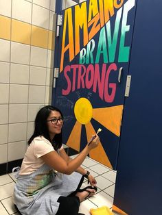 a woman sitting on the floor in front of a sign that reads amazing brave strong