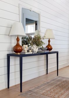 a console table with two lamps and a mirror on it in front of a white wall