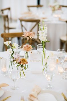 the table is set with white and pink flowers in vases, plates and napkins