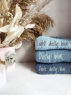 three towels with words written on them sitting next to some dried flowers and a vase