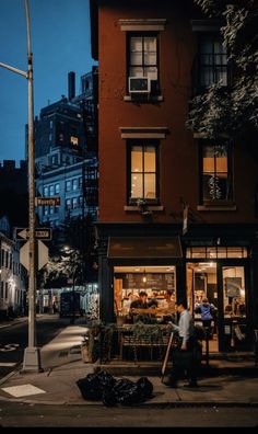 a person walking past a store on the side of a city street at night with buildings in the background