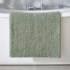 a green towel hanging on the side of a bath tub