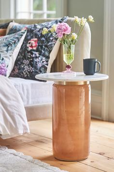 a vase with flowers on top of a table next to a couch and coffee cup