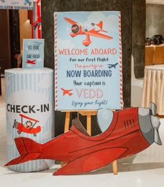 an airplane themed welcome sign next to two cardboards that read,'welcome aboard now boarding your captain is ved enjoy your flight '