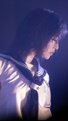 a woman with dark hair wearing a white shirt and black tie, standing in the dark