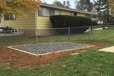 a house behind a chain link fence with gravel on the ground in front of it