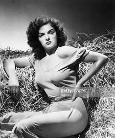 an old photo of a woman sitting in hay with her hands on her hips and looking at the camera