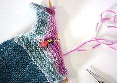 a pair of scissors next to a knitted object on a white table with yarn