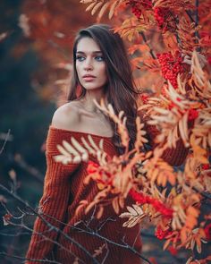 a beautiful young woman standing next to a tree with red berries on it's branches