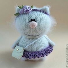 a knitted teddy bear wearing a purple skirt and flower headband with a tag